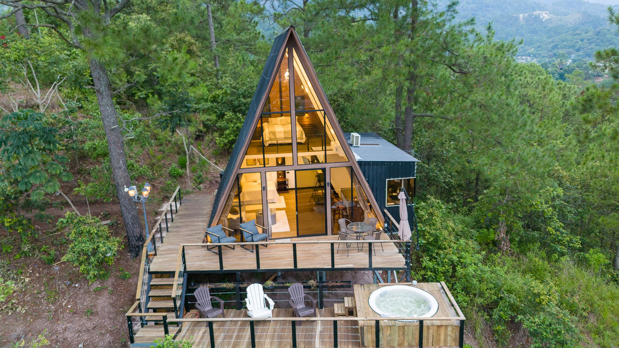Cabaña A-frame de La Vista iluminada al atardecer entre pinos, vista desde un dron