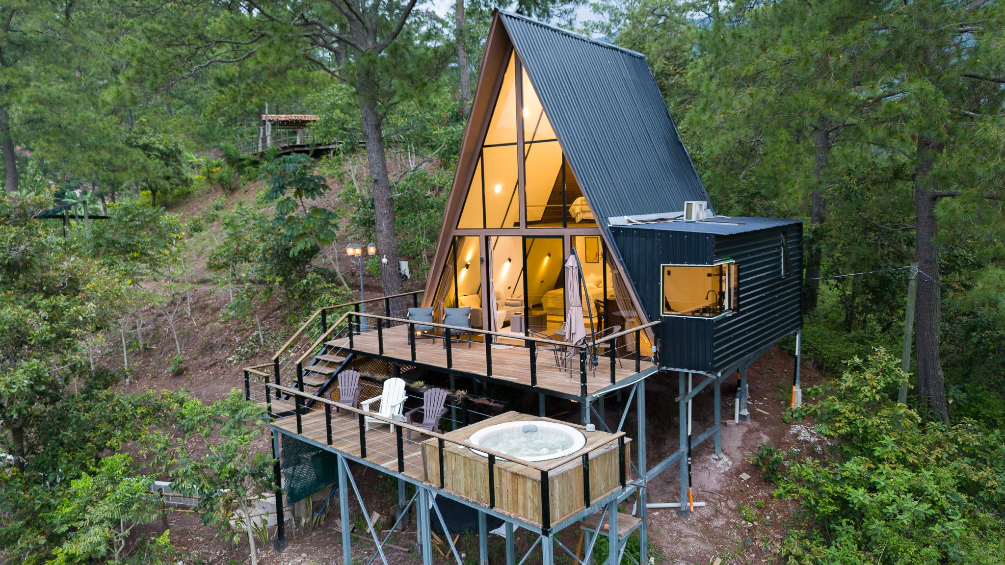 Vista aérea de la cabaña con su deck y jacuzzi entre pinos