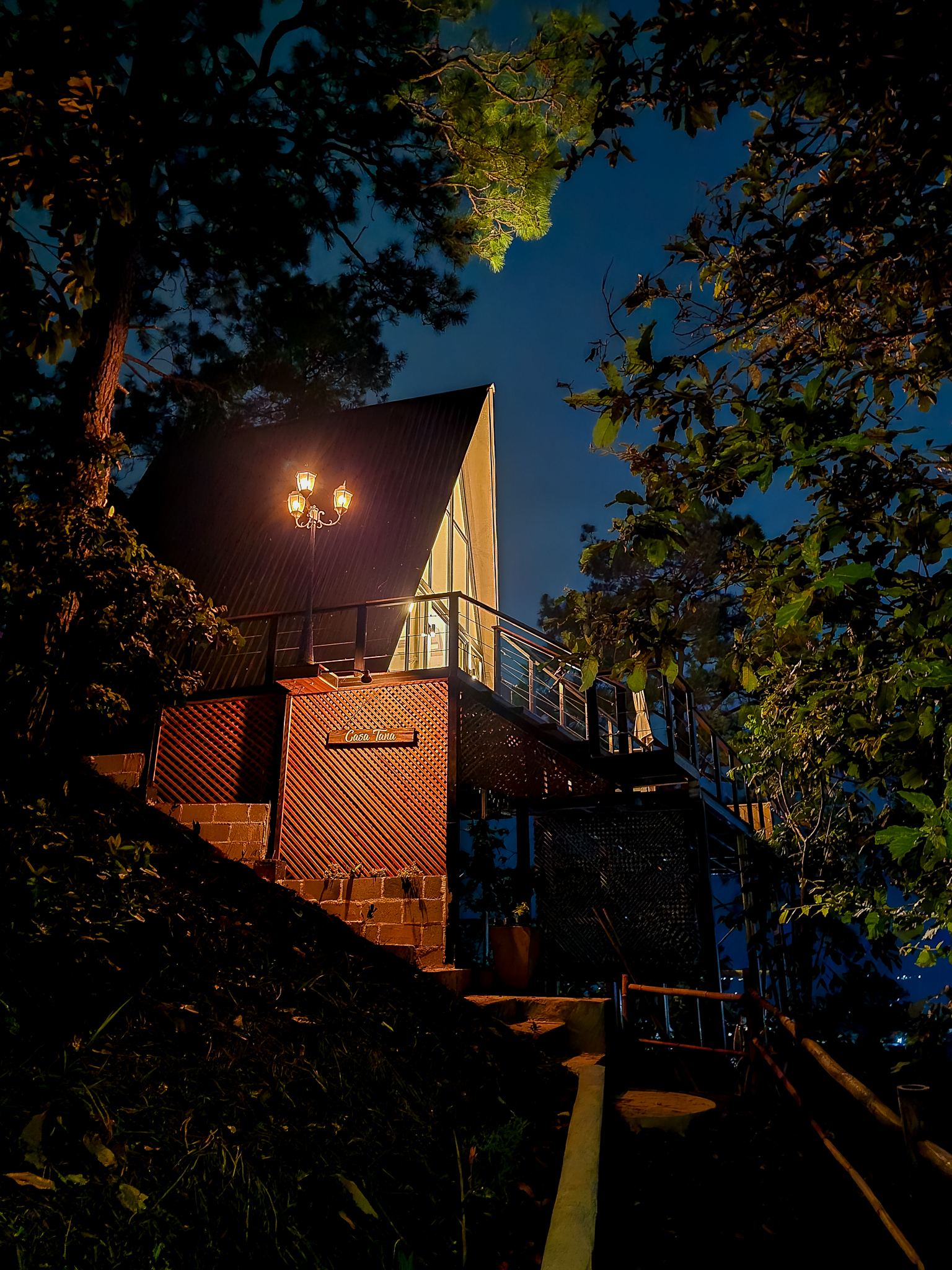 Cabaña A-frame de noche entre árboles, con terrazas iluminadas